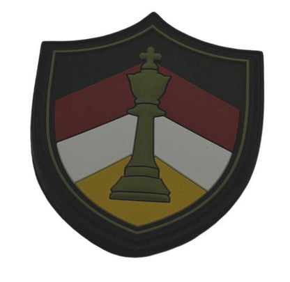 A shield-shaped patch featuring a green chess king centered over diagonal red, white, and yellow sections on a black background, isolated on a white backdrop.